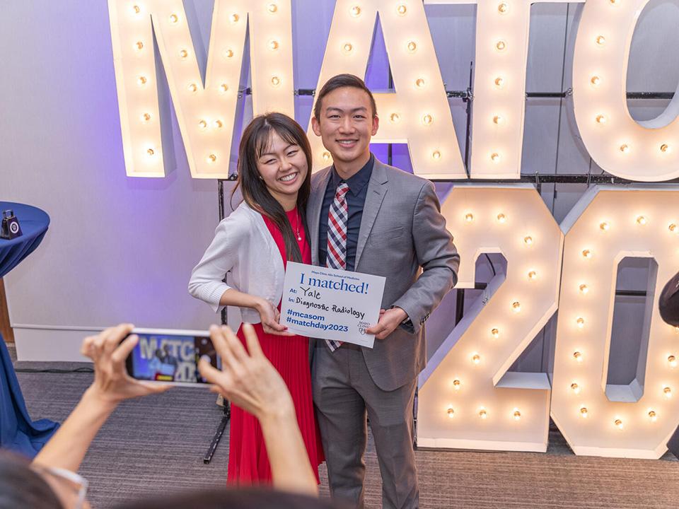 Med student and loved one pose for a picture in front of the Match Day sign