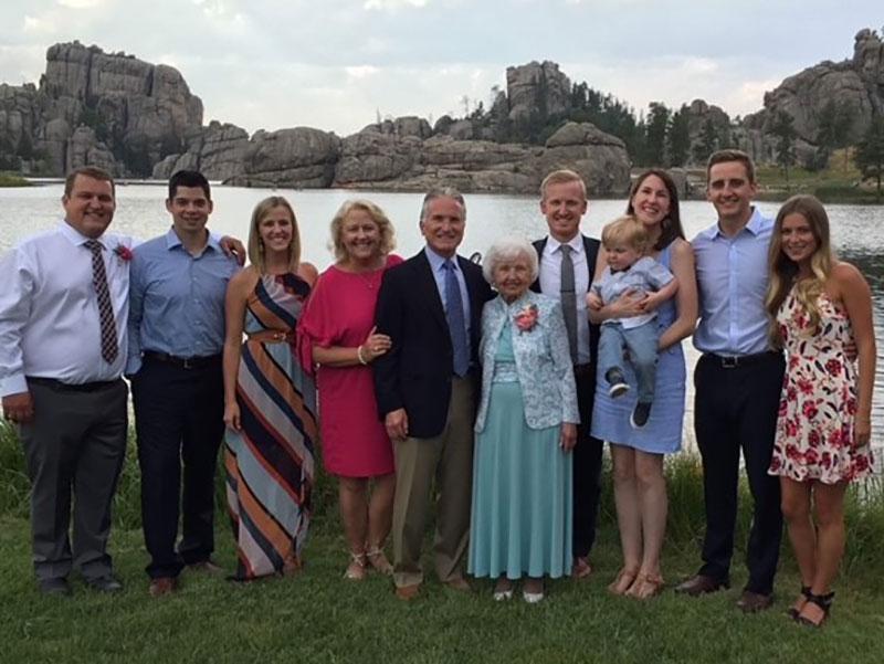Faculty stand together with family for a picture with a mountain backdrop.