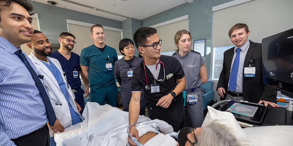 A medical student performs a chest ultrasound on a patient in a simulation setting while others observe