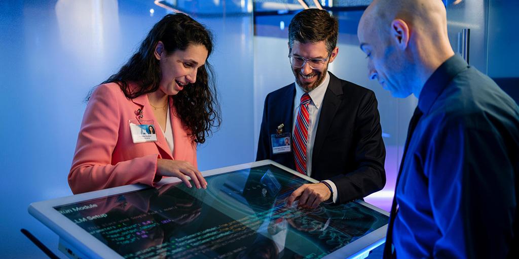 Members of the Otolaryngology Artificial Intelligence (ENT AI) team work together while gathered around a large touch screen tablet, displaying code on the screen.