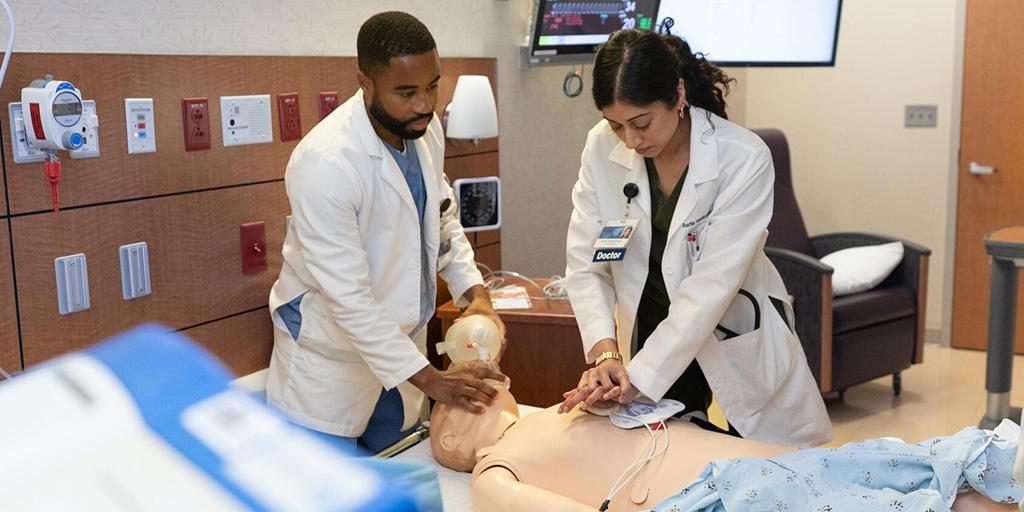 An Internal Medicine resident uses a manual resuscitator on a medical training mannequin while another resident performs chest compressions