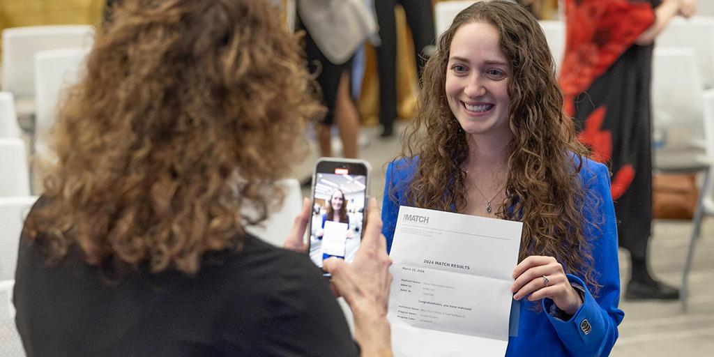 Shalyn Fullerton holds her match letter and poses for a picture being taken with a smartphone during Mayo Clinic Match Day.