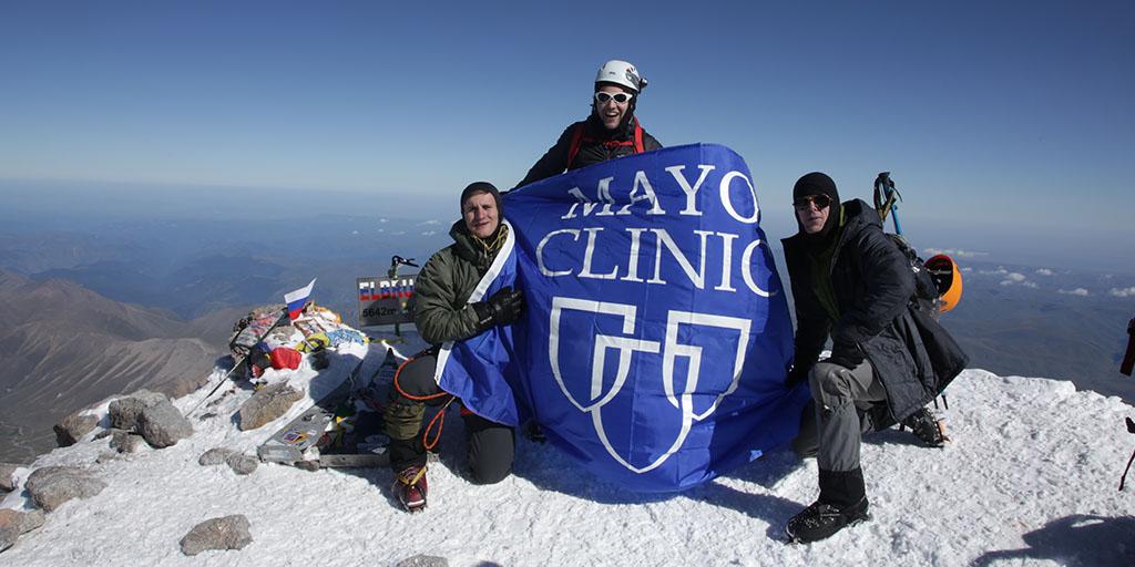 Three medical students holding Mayo Clinic flag atop Mount Elbrus