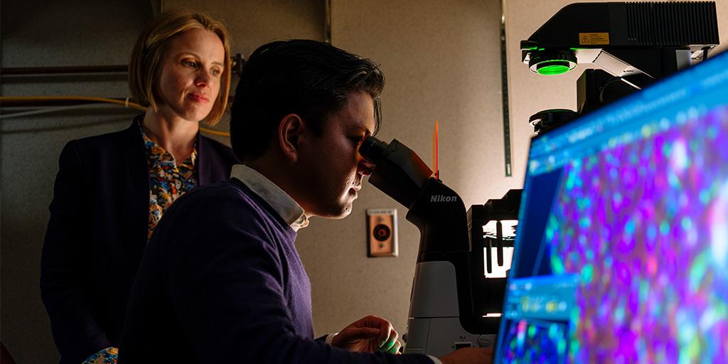 Researcher views microscope with mentor