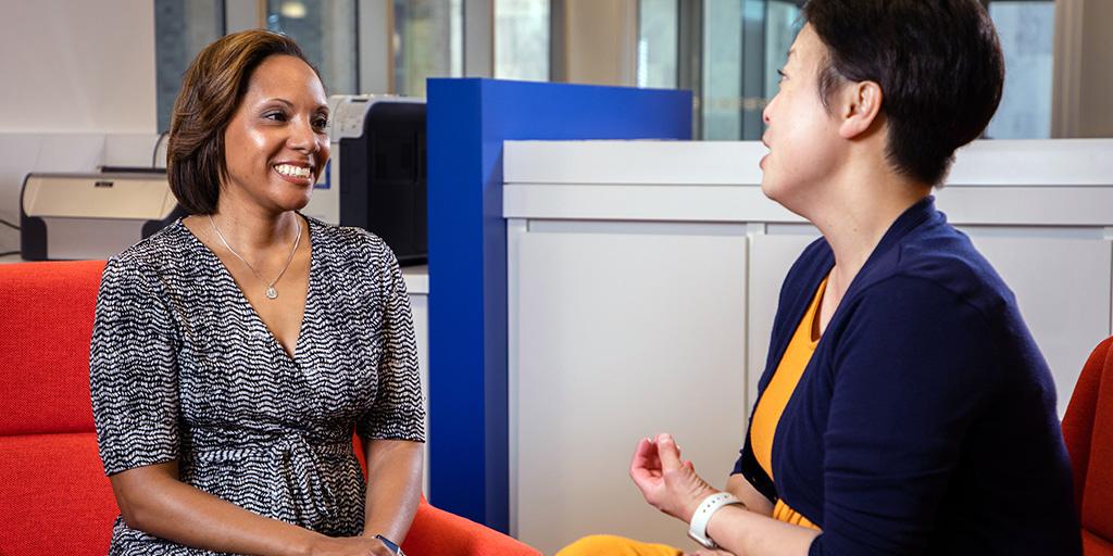 Two female financial aid mentors facing and talking to each other at a table in a library type setting.