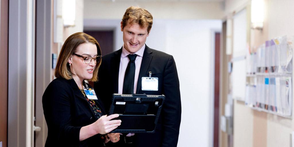 Two doctors look at table screen together in a hallway.
