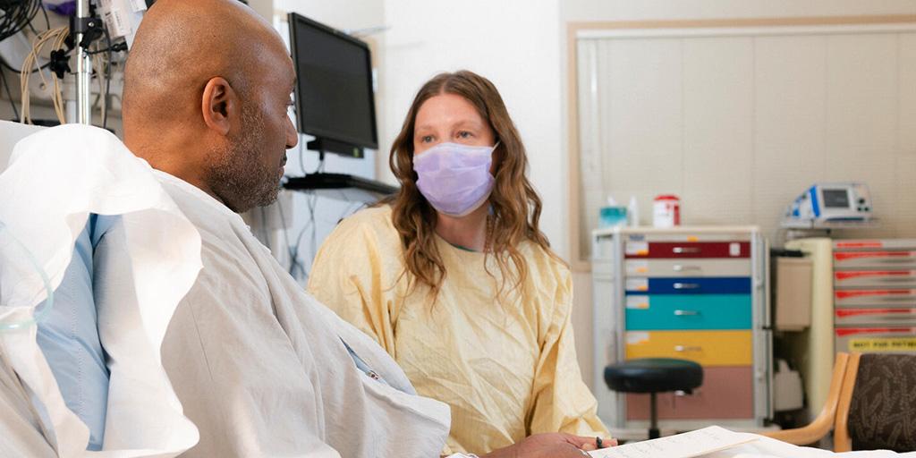 A nurse talking with a patient in a hospital bed.