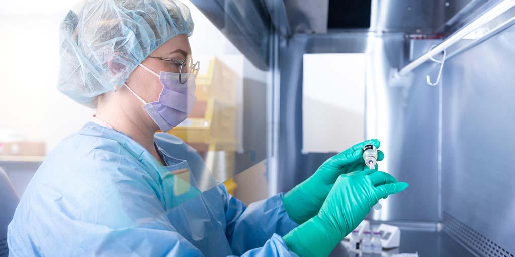 A technicians works with a vial of IV medication.