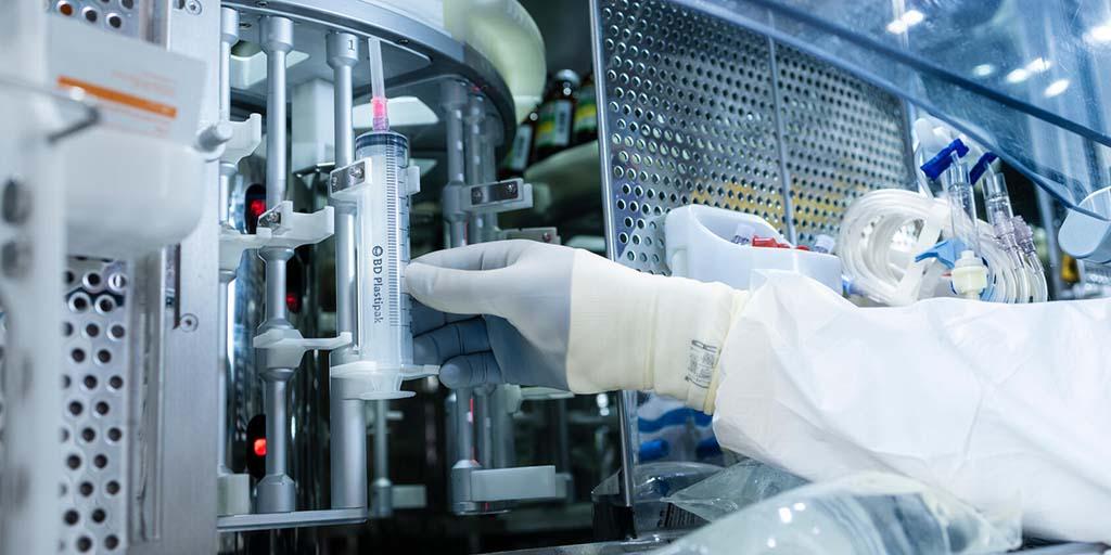 The gloved hand of a technician reaches into an IV solution automation machine.