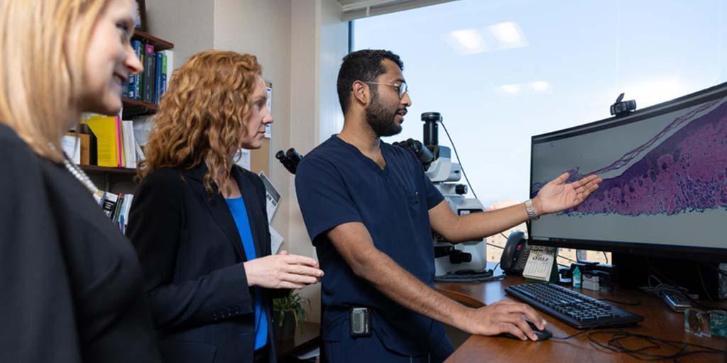 Maniam Ganesh, MD, MBA, Dermatology resident, reviews a pathology slide image on a screen with Carilyn Wieland, MD, Dermatology consultant and Dermatology Residency program director, while another resident observes