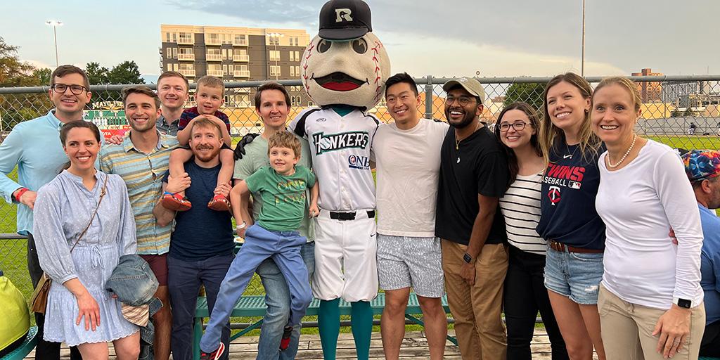 Thirteen adults and children gathered at a baseball field with the Rochester Honkers' mascot for a group photo.