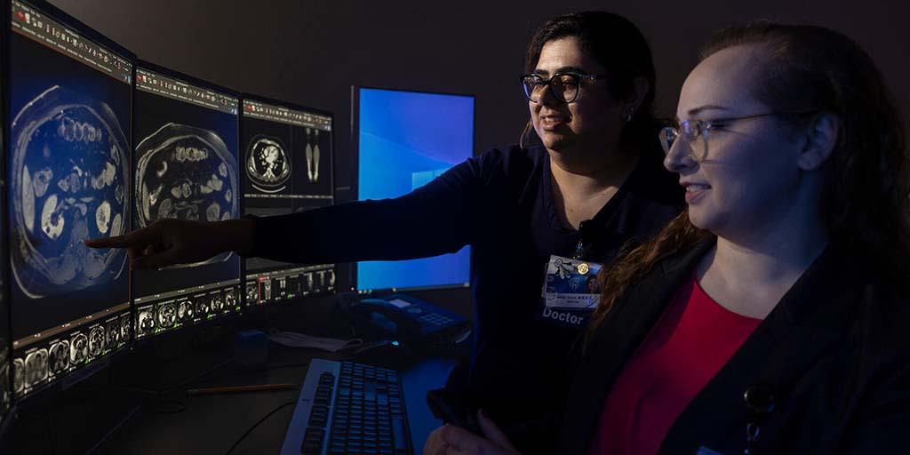 Two diagnostic radiologists review medical imaging on a computer monitor together.