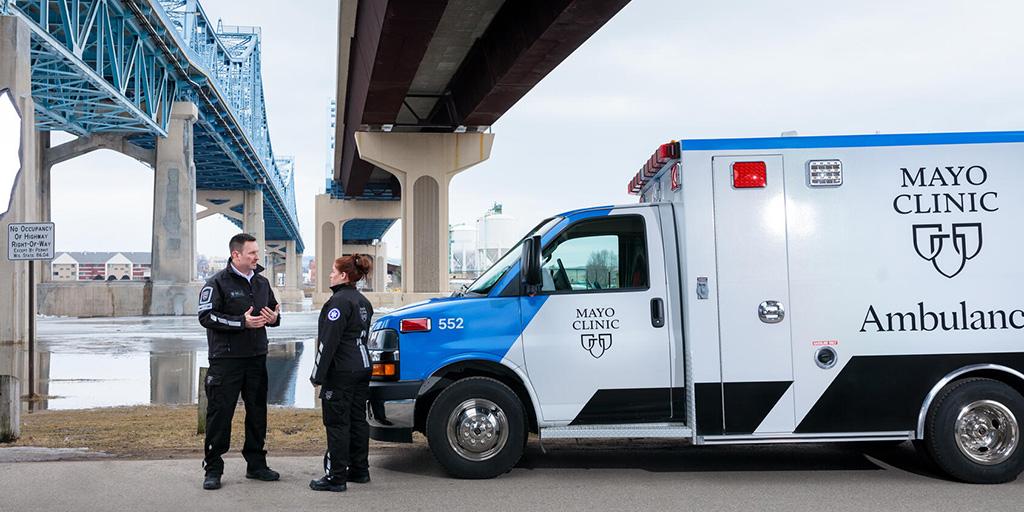 Two paramedics standing next to a Mayo Clinic ambulance under a bridge