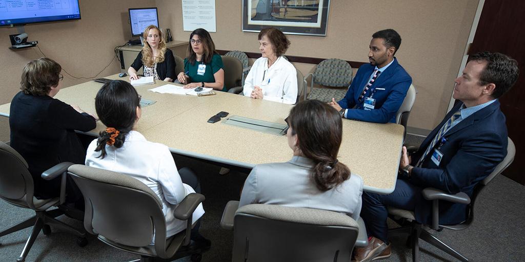 Eight doctors sitting at a table in a conference room having a discussion.