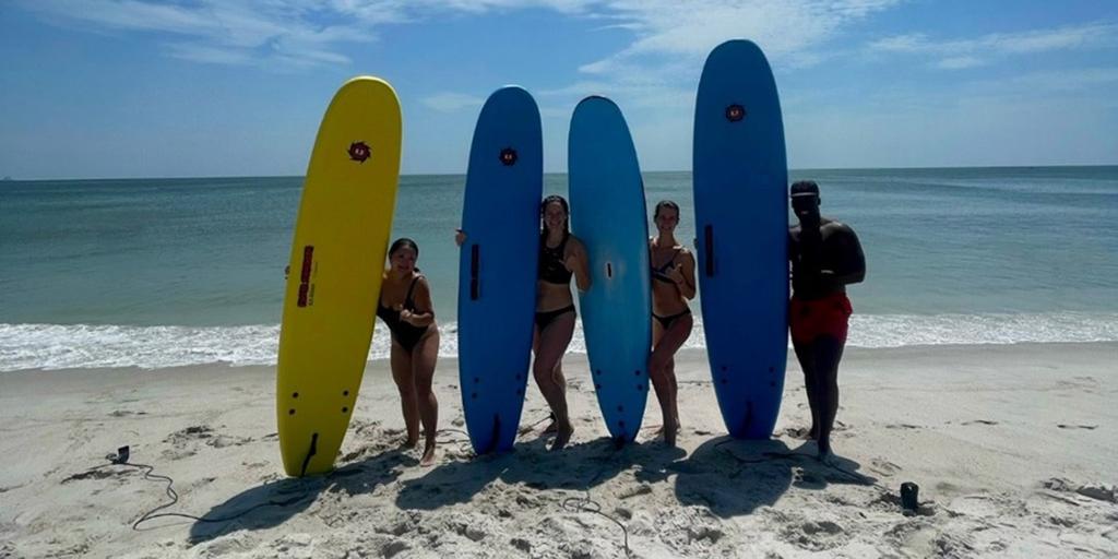 Four residents pose with surfboards on beach.