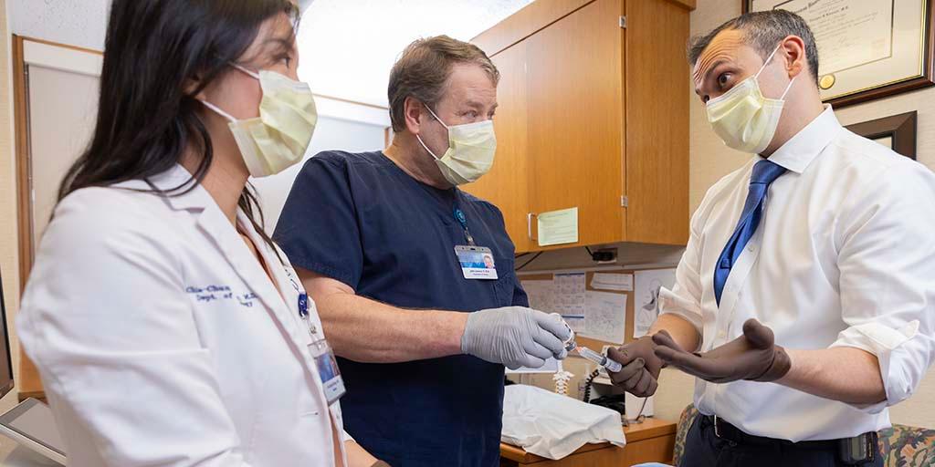 Two neurology consultants and a nurse, all wearing gloves and surgical masks, work together to prepare a procedural tray.