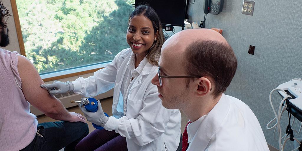 Two internal medicine residents conduct a procedure on a patient arm.