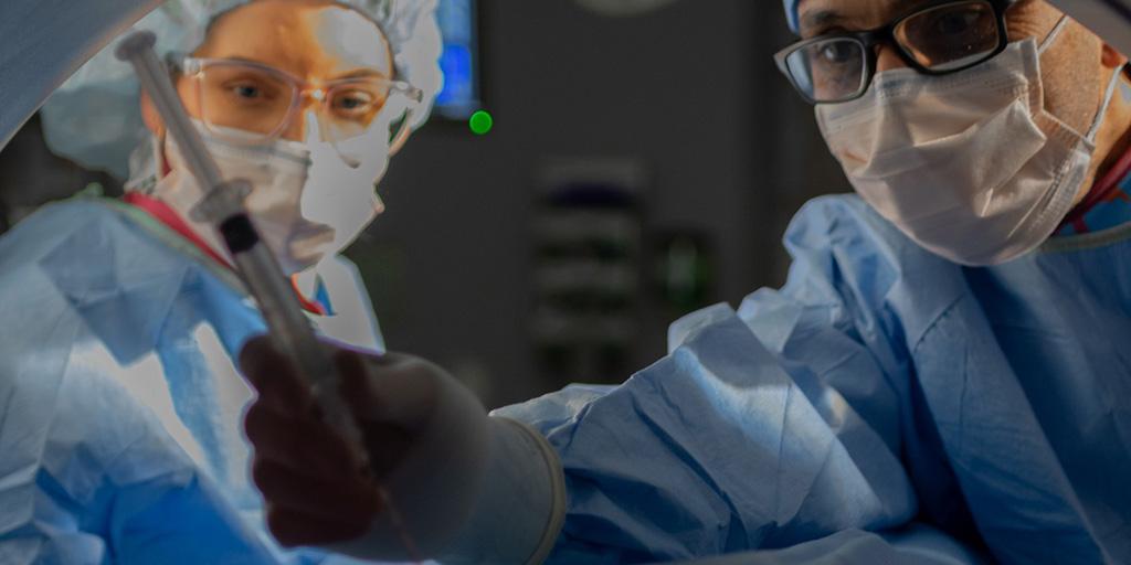 Two respdents perfoming simulated surgery in surgery suite in scanning device.