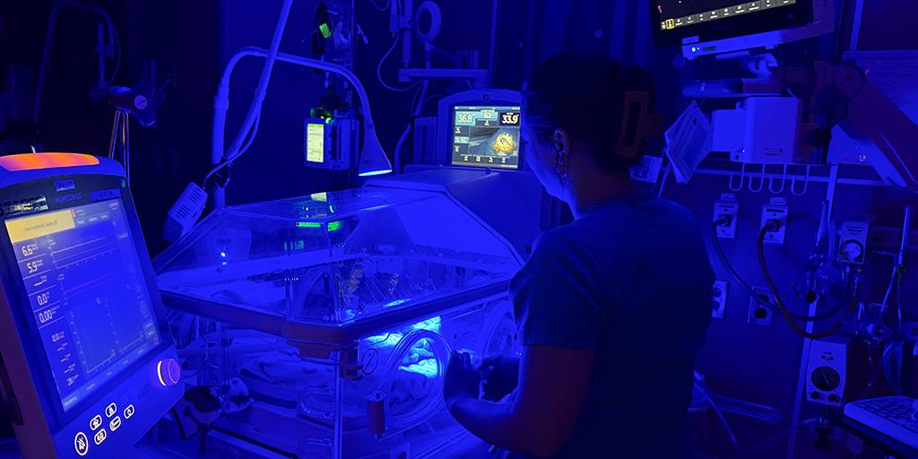 A nurse checks on a baby in a dark room.