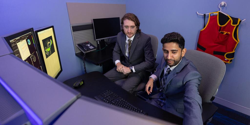 Two people from the Neuroradiology Fellowship program in Jacksonville, Florida, sitting at a desk and looking at multiple computer monitors.