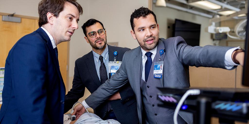 Three doctors in an exam room performing an ultrasound on a patient.