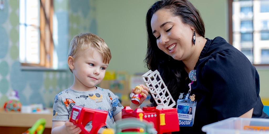 A doctor works with a child while sitting at a child's table with toys.