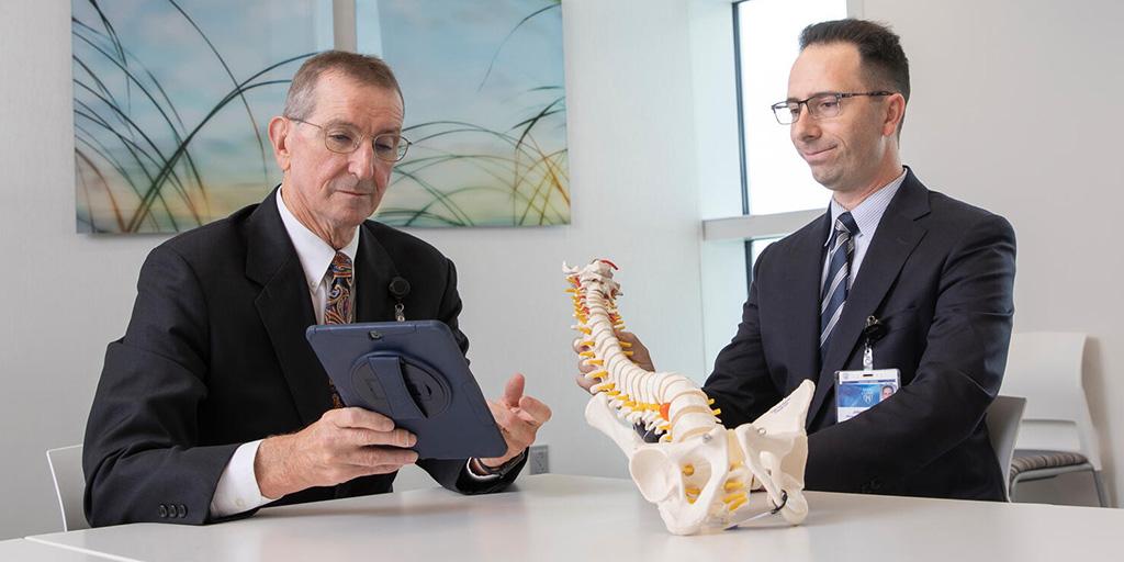 Physical Medicine and Rehabilitation doctors observe a tablet and discuss an anatomical spine model in a conference room.