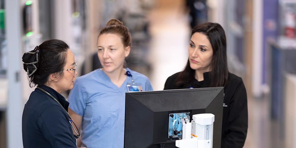 Three fellows from Pulmonary and Critical Care Medicine Fellowship look at computer stand in hallway.
