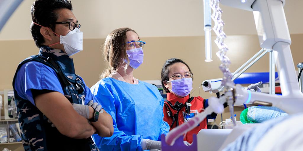 Three fellows in patient room looking at machinery.