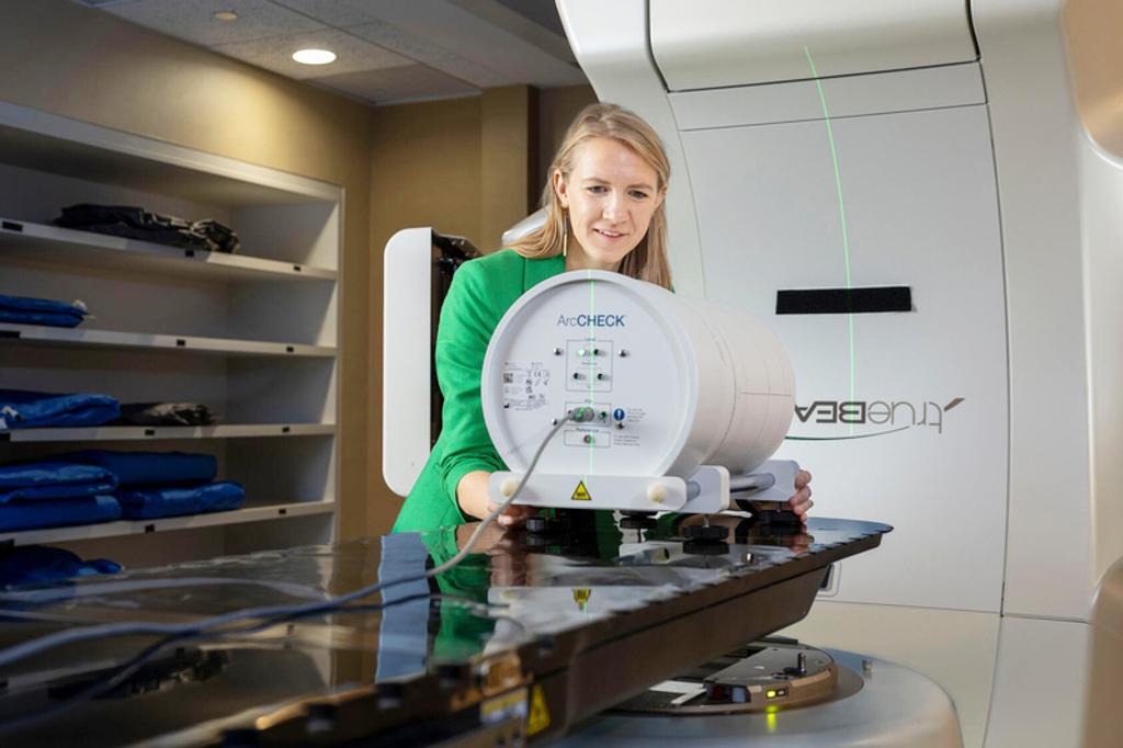 A person in a radiology room demonstrating use of the ArcCHECK radiology imaging machine.