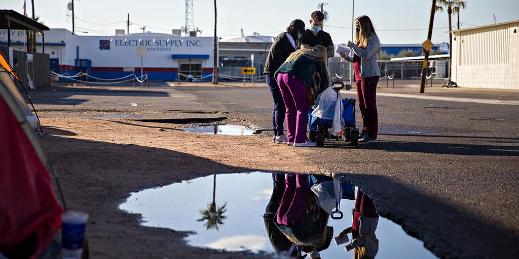 A group of medical students and volunteers with Street Medicine Phoenix gather around a patient
