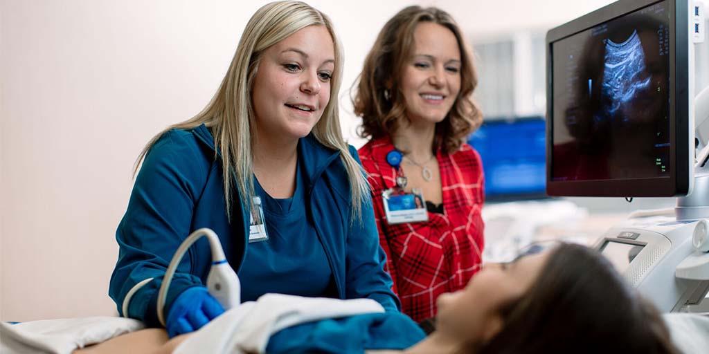 A sonography student performing an ultrasound on a patient with a faculty member overlooking