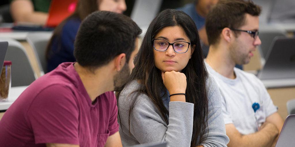 Group of students in a lecture hall, working in groups of two and discussing problem