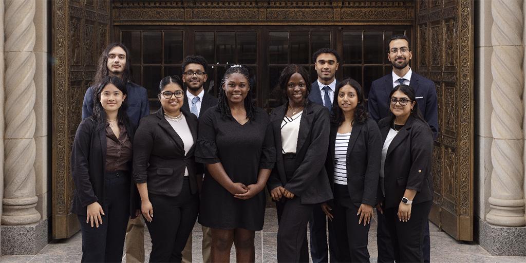 Undergraduate Plummer Scholars (UPS) program formal group portrait of 10 people standing in front of the Plummer building doors.