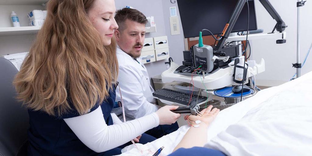 A technician is guided by her instructor during a nerve conduction studies clinical lab session for the Clinical Neurophysiology Technology (CNT) program.