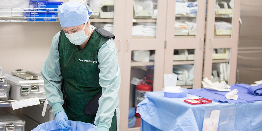 Nurse wearing surgical scrubs and mask in an operating room preparing tools on a table