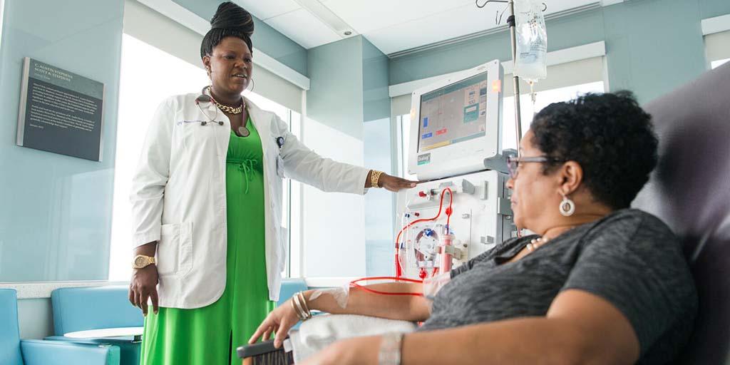 One provider standing near a dialysis machine in a hospital setting, chatting with a patient