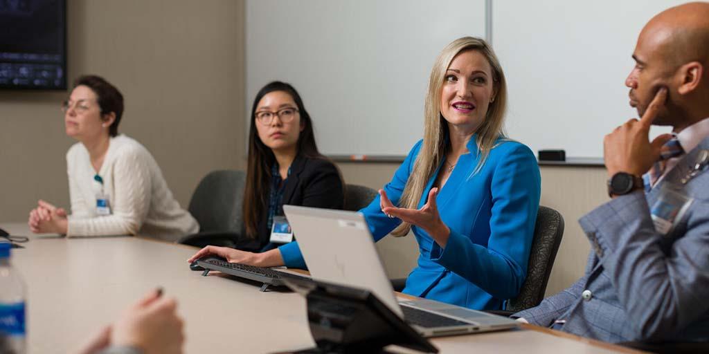 Group of students sitting around a table discussing something on a laptop computer screen