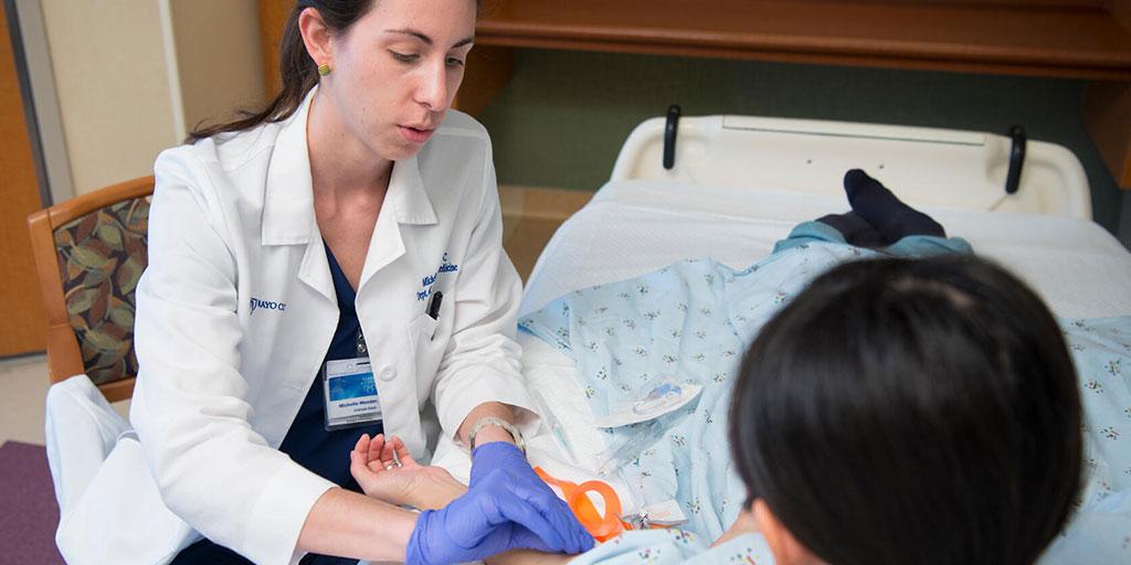 Fellow with patient laying on exam table inserting an IV