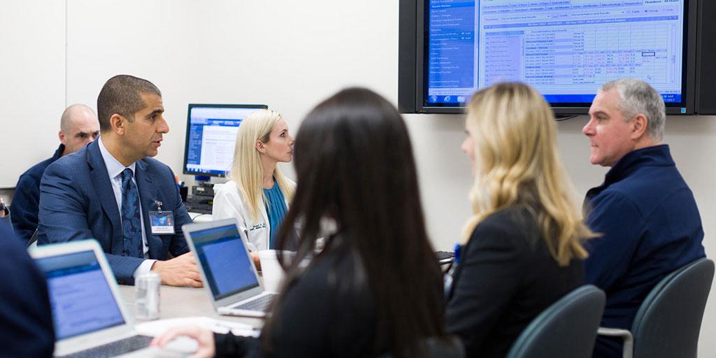 Group of fellows sitting around computer in classroom studying cases
