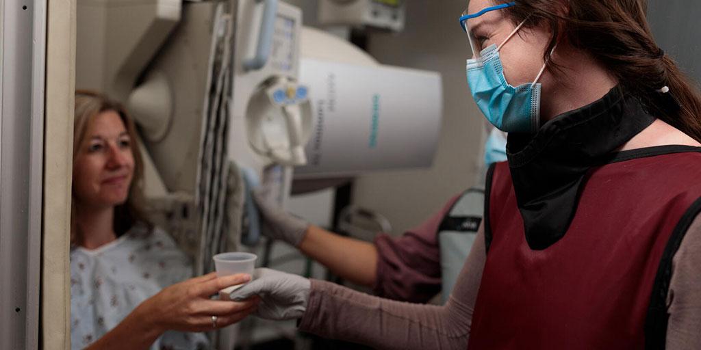 Occupational therapist in mask handing patient thickened water in an exam room
