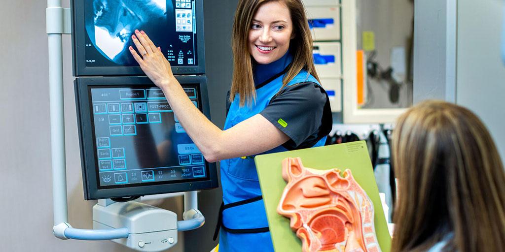 Occupational therapist in an exam room with patient, showing them something on a screen while the patient looks at a diagram of the anatomy of the throat.