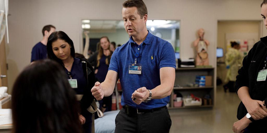 Room full of students with faculty in OT standing in the middle of the classroom