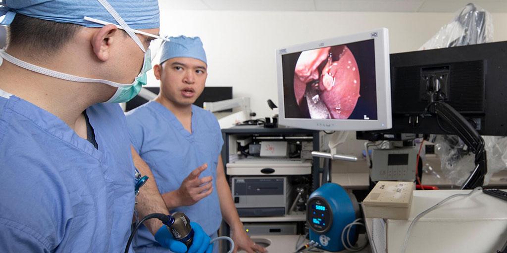 Two fellows wearing scrubs in a simulation room with computer screens looking at the inside of a throat