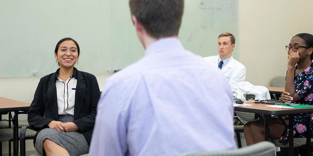 Group of students in a classroom, sitting at tables, but looking at each other and discussing something