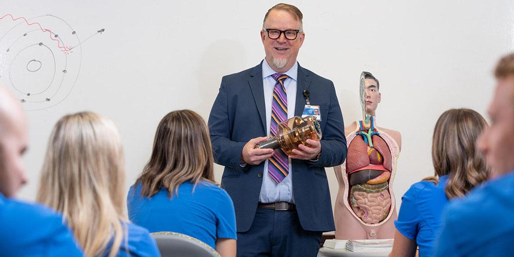 An instructor holds an X-ray tube in front of a class of radiography students.
