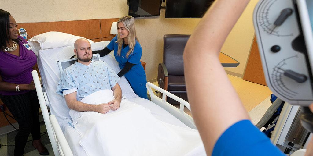 Radiography students position a practice patient in a hospital bed for an X-ray