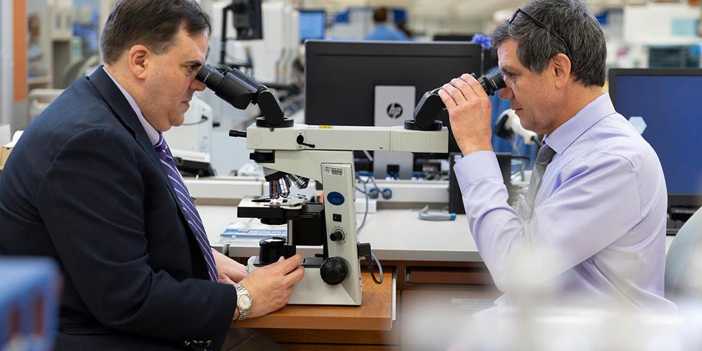 Two people from the Anatomic and Clinical Pathology Residency program at Mayo Clinic in Jacksonville, Florida, sat at a desk across from each using a dual-head microscope.