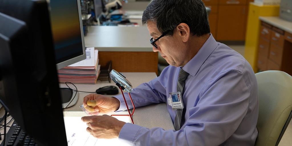 A person from the Anatomic and Clinical Pathology Residency program at Mayo Clinic in Jacksonville, Florida, sat at their desk and viewed a readout over a lightbox.