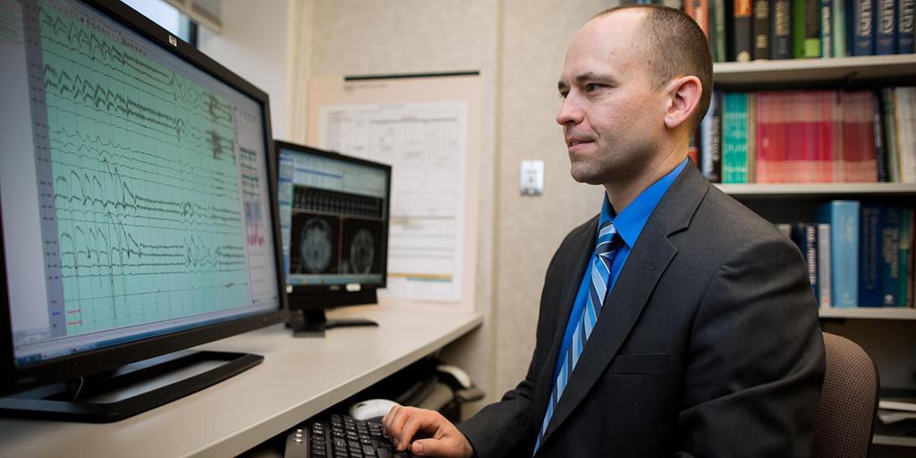 Brian Lundstrom, M.D., Ph.D. at a computer desk looking at a computer monitor.